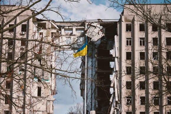 Flag of Ukraine against the background of a destroyed building i The Russian military’s actions amount to two crimes against humanity.